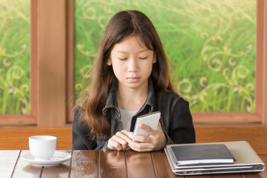Asian young girl using mobile phone while sitting at desk