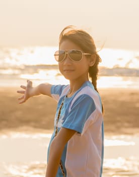 Girl with sunglasses and open arms under the sunrise at seaside
