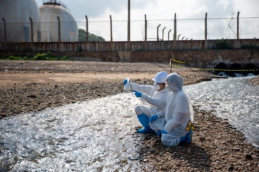 Ecologist sampling water toxic chemicals from river with test tube glass and have white smoke, Biologist wear protective suit and mask collects sample waste water from industrial, problem environment
