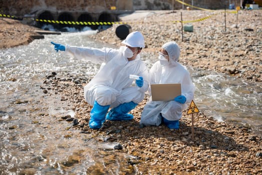 Biologist wear protective suit and mask collects sample of waste water from industry, problem environment, Ecologist sample taken dead fish to inspection and save data to laptop computer, Toxic water
