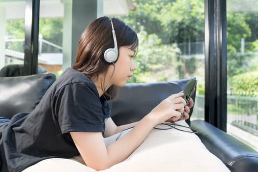 Young girl with headphones and listening to music from mobile phone on the sofa in living room at home