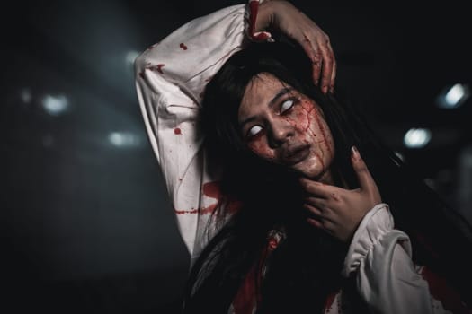 Screaming zombie female face with blood grabs her head to twist it off, Horror bloodthirsty woman ghost or zombie she is horror scary with breaks her neck at dark night, Happy halloween day concept