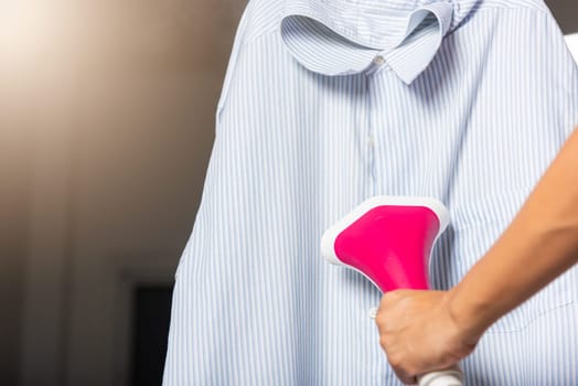 Close up of woman using electric hand steam generator while it is hot and steam comes out for clothes shirt at house, Household & home equipment for housework, concept of linen care