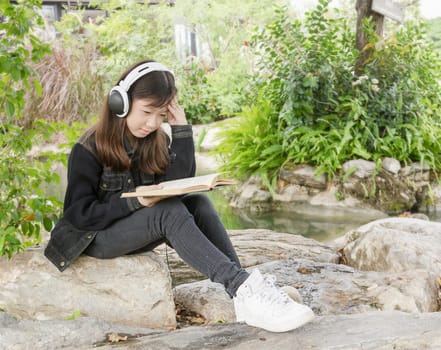 Young beautiful girl reading a book and .listen to music at the park