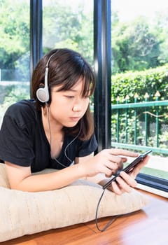 Teenage girl with headphones and listening to music from mobile phone at home