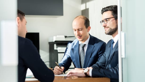 Team of confident successful business people reviewing and signing a contract to seal the deal at business meeting in modern corporate office. Business and entrepreneurship concept.