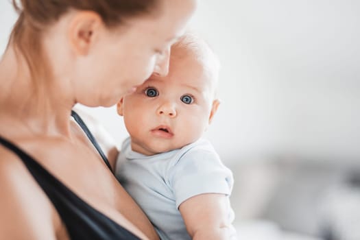 Portrait of sweet baby resting in mothers arms, looking at camera. New mom holding and cuddling little kid, embracing child with tenderness, love, care. Motherhood concept.
