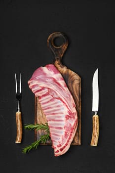 Top view of raw fresh lamb ribs, uncut with fork and knife for grilling