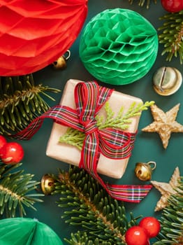 Wrapped gift boxes between Christmas decorations and green fir branches top view on green background. Christmas or New Year Holiday atmosphere flat lay