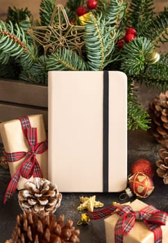 Hardcover notebook between decorations, fir branches and pine cones close up, mockup. Christmas or New Year greeting card template, Holiday or wedding stationery
