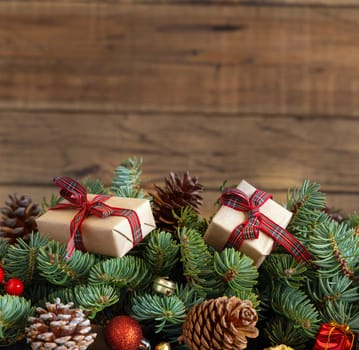 Wrapped gift boxes on reen fir branches near Christmas decorations and pine cones close up on wooden background, copy space. Christmas or New Year Holiday atmosphere