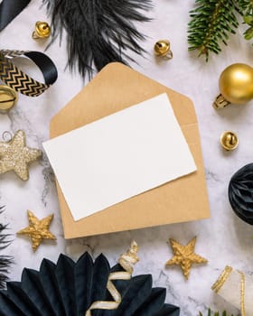 Paper card and envelope between black and golden Christmas decorations and fir tree branches top view. Winter flat lay with blank invitation card, Mockup, copy space