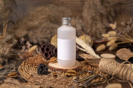 Cosmetic bottle with blank label on wood near natural decorations close up, package mockup. Eco friendly skincare product, lotion or cream. Bohemian composition with dried leaves and flowers.