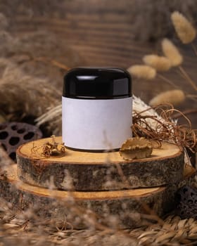 Cream jar with blank label on wood near natural decorations close up, package mockup. Eco friendly skincare product, lotion or cream. Bohemian composition with dried leaves and flowers.