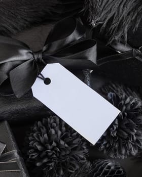 Wrapped Gift Boxes with black paper flowers and decorations and rectangular gift tag, mockup, copy space. Dark composition with blank label card for Birthday, Anniversary or black party present