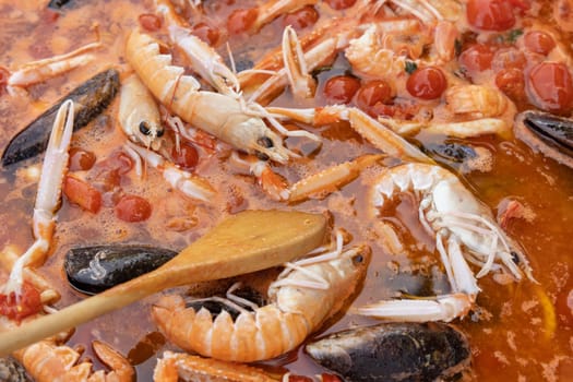 Cooking Italian spaghetti allo scoglio, pasta with seafood and tomatoes close up in a frying pan. Mediterranean Apulian traditional food with fresh stewed clams, shrimps, mussels, octopus and squid