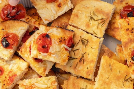 Freshly baked homemade apulian focaccia cut in slices top view. Barese focaccia with tomatoes, rosemary, extra virgin olive oil and salt flakes. Italian Mediterranean traditional food