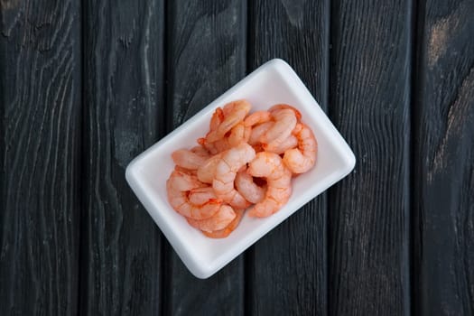 Small boiled peeled shrimps in small plate on dark wooden background. Top view.
