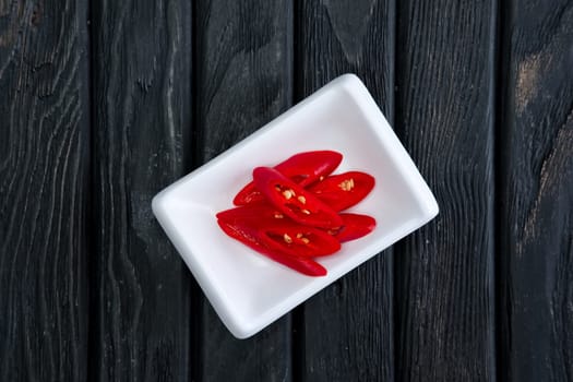 Pieces of chilli in plate on dark wooden background. Top view.