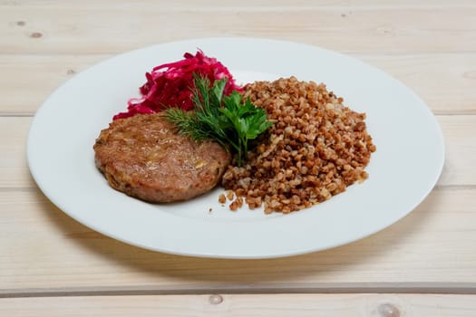 Portion of fried beef cutlet, boiled buckwheat and pickled red cabbage