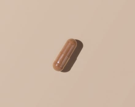 Brown medical capsule on light beige top view, hard shadows. Preventive medicine and healthcare, taking dietary supplements and vitamins. Minimal composition