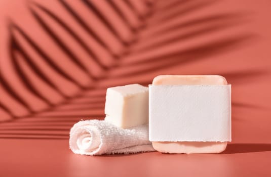 Handmade soap bars with blank label and small face towel on pink close up, palm leaf hard shadows. Skincare beauty product package. Exotic natural cosmetics, pastel minimal composition..