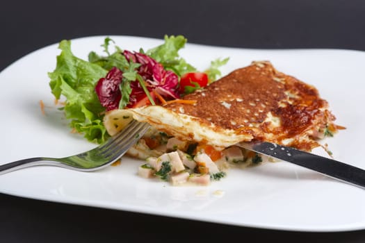 Cutting with knife omelet with ham and vegetables