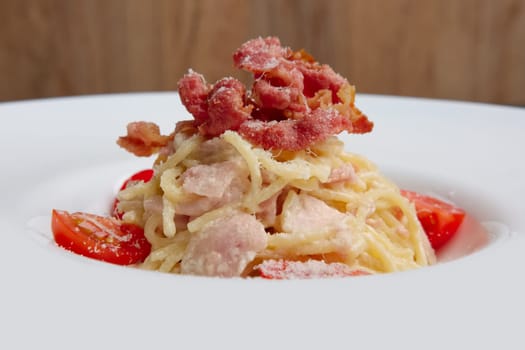 Plate with pasta served with bacon and ham, decorated with tomato cherry, closeup