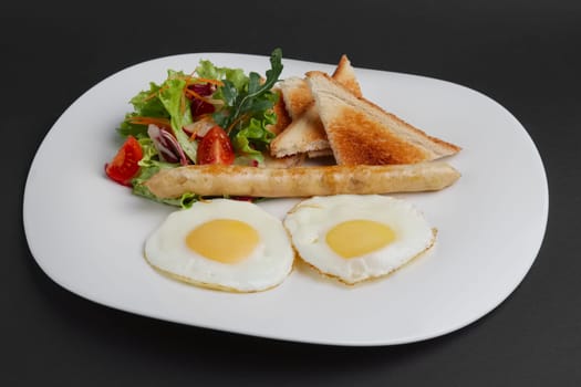 Fried eggs with homemade sausage, toasts and fresh tomato and salad on a plate