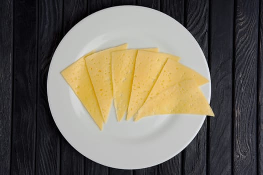 Top view of cheese slices on round plate on wooden table.