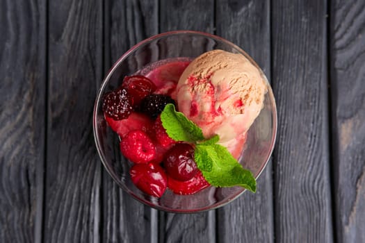 A cup of cherry ice cream decorated with raspberries and dewberry and mint leaves. Top view.
