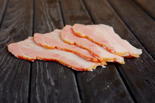 Selective focus photo of slices of fresh bacon on wooden table.