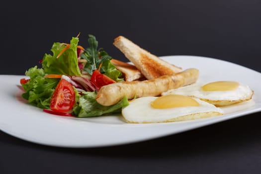 Closeup view of fried eggs with homemade sausage, toasts and fresh tomato and salad.