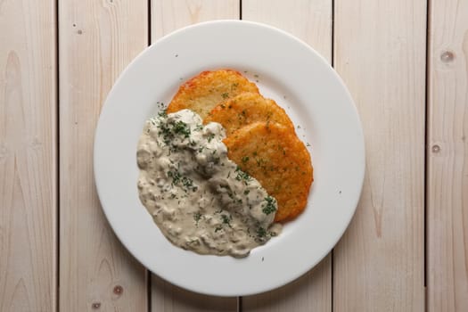 Traditional belorussian potato pancakes draniki with mushroom sauce on a plate