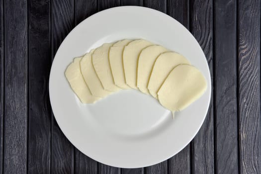 Top view of mozzarella  cheese slices on round plate on wooden table.
