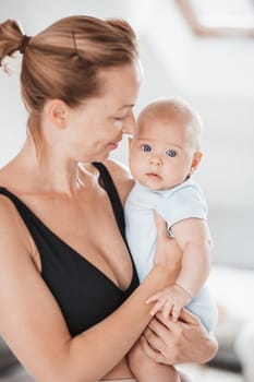 Portrait of sweet baby resting in mothers arms, looking at camera. New mom holding and cuddling little kid, embracing child with tenderness, love, care. Motherhood concept.