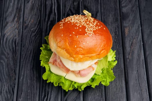 Top view of big Egg burger with mozzarella, salad, and fried bacon on dark wooden table