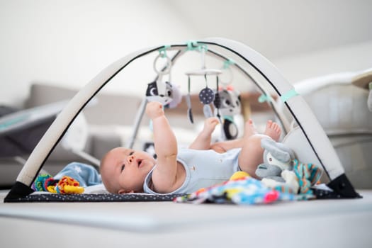 Cute baby boy playing with hanging toys arch on mat at home Baby activity and play center for early infant development. Baby playing at home.