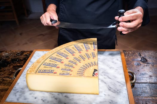 July 11 2022, Lyon, France : A man cuts a portion of The Gruyère with a wire, the famous swiss cheese in a cellar on a marbble background
