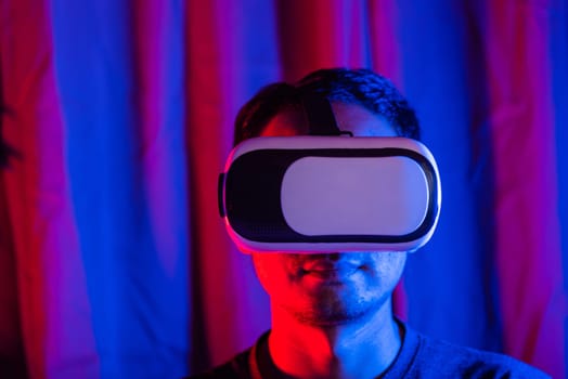 Asian handsome man wear VR helmet excited emotional at home purple and blue background, experiencing virtual reality goggles experiencing reality excited emotional, metaverse and cyberspace