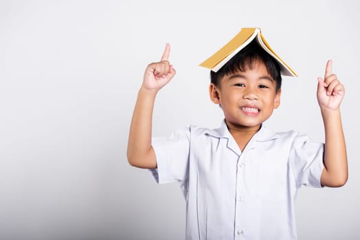 Asian adorable toddler smiling happy wearing student thai uniform red pants stand holding book over head like roof in studio shot isolated on white background, Portrait little children boy preschool