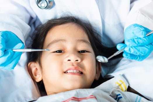 Dental kid health examination. Doctor examines oral cavity of little child uses mouth mirror to checking teeth cavity, Asian dentist making examination procedure for smiling cute little girl