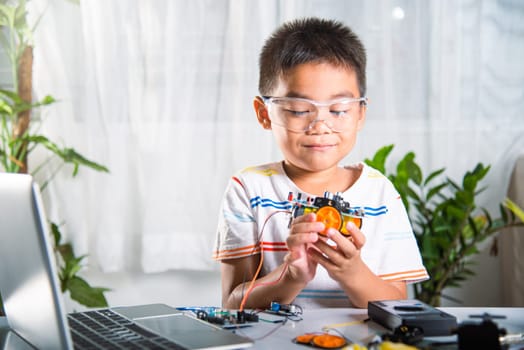 Little child trying assemble build wheel to car toy, Asian kid boy assembling wheel into Arduino robot car homework, creating electronic AI technology workshop online school lesson