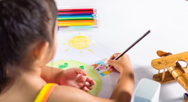 Happy child little girl colorful drawing family standing hold hands on planet earth on paper, Asian cute kid preschooler sit on table smiling she draw picture with pencil at home, earth day concept