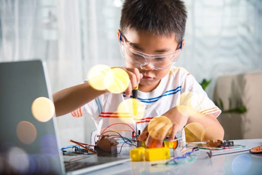 Little child tighten the nut with a screwdriver to assemble car toy, Asian kid boy assembling the Arduino robot car homework project at home, education AI technology workshop school learning lesson