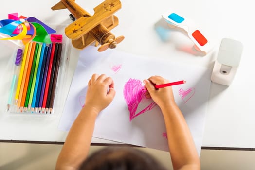 Happy child little girl colorful drawing pink heart on white paper, Asian cute kid preschooler smiling draw color love picture card at home, Valentine's or Mother's Day or Father's Day