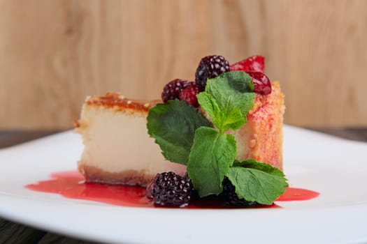 Piece of cheesecake with cherry, strawberry.and dewberry decorated with syrup and mint leaves on table