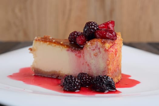 Piece of cheesecake with cherry, strawberry and dewberry decorated with syrup