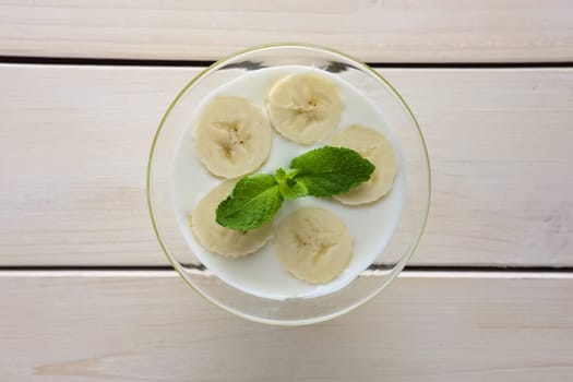 Top view of glass with yogurt and raw honey topped with sliced bananas and mint leaf. Selective focus photo.