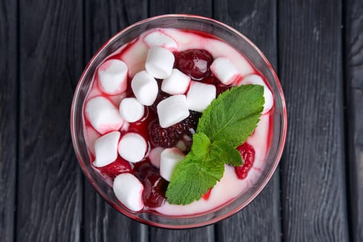 A glass of youghurt with marshmallow and raspberries decorated with mint leaves. Top view.